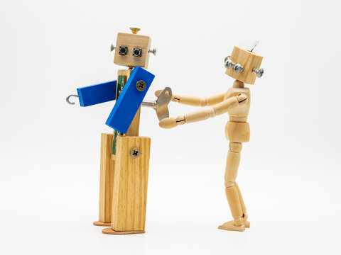 Peque&ntilde;os robots hechos con madera y tornillos girando llave de cuerda, aislado en blanco