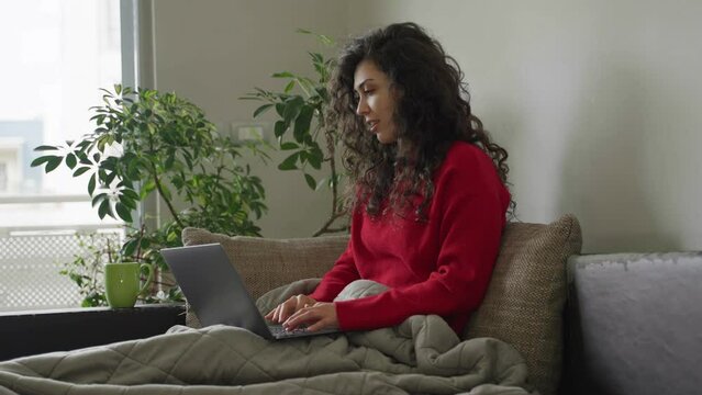Curly hair brunette woman working on a laptop from home, sitting on a couch and smiling with a mug of tea, with window and plant in the background.
4K, 50fps, 10bit from FX3 in Slog3
