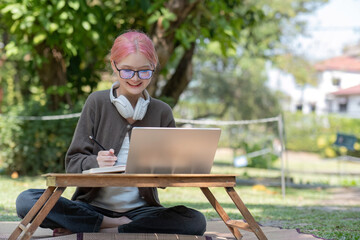 Asian female student studying online Happy woman looking at computer screen Surf the web or do video chat on webcam. Happy woman using laptop and wearing headphones sitting in the park