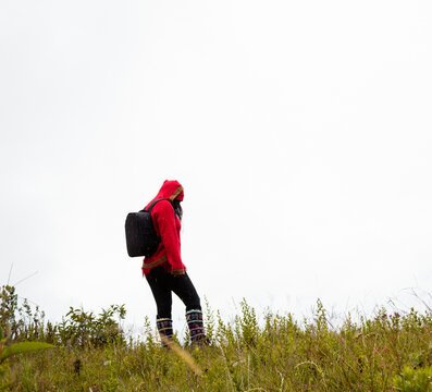 Explorando el invierno Chica con mochila y chompa rojo disfrutando del paisaje campestre bajo un cielo nublado,turista viajero,estilo de vida