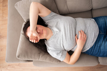 Fototapeta premium Peaceful woman lying on back on comfortable couch at home, covering eyes with hand, sleeping at daytime, feeling tired, enjoying relaxation, leisure, break, weekend. Top view