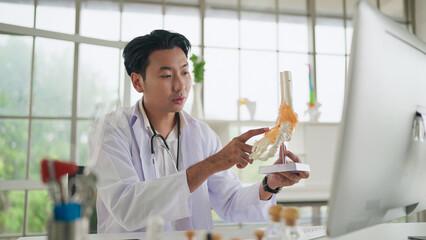 Online medical consultation. Asian male orthopedic doctor showing foot skeleton, ankle joint...