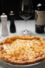 Khachapuri with cheese serving on table with red wine, megrelian khachapuri on white plate, concept of georgian cuisine menu.