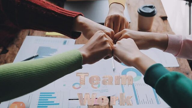 Equipo de trabajo uniendo sus manos festejando el trabajo en grupo, sobre escritorio con gráficos de barras, taza de café., coloridos pullovers. Teamwork titilante tallado en madera 