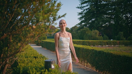 Carefree woman strolling bushes on garden pathway. Girl enjoying park greenery