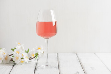 A glass of rose wine with a decorative flowering cherry branch on a white wooden table. Side view, selective focus. Pink wine. - 753698300