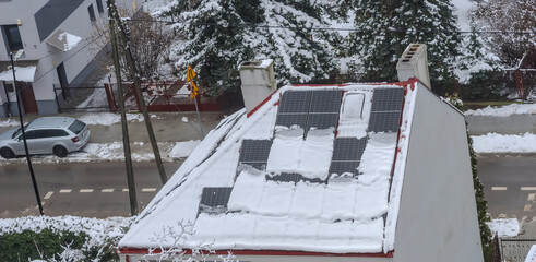 Panele słoneczne na dachu domu pokrytego śniegiem.Miasto po lekkich opadach śniegu w lutowe południe przyprószone śniegiem jak cukrem pudrem. - obrazy, fototapety, plakaty