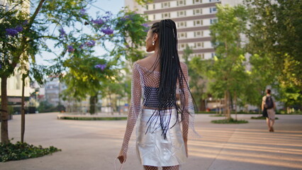 Fototapeta premium Relaxed brunette walking city back view. African girl enjoying summer stroll