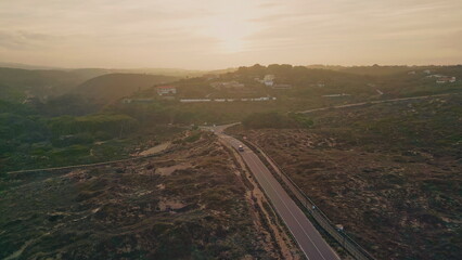 Beautiful sunset road passing green valley aerial view. Straight asphalt roadway