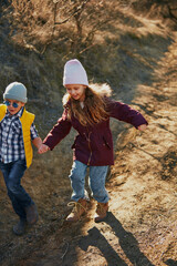 Smiling children, boy and girl, in colorful jackets leading friends on hike in wilderness. Concept of outdoor activities for children's development, school, childhood, fashion and style. Ad