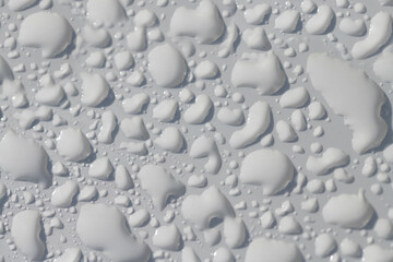Close-up, background and close-up of a white lacquered surface on which many water pearls shimmer.