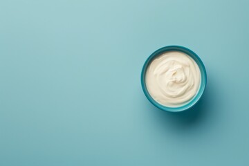 Yogurt is presented in a blue bowl on a blue background, captured from an aerial view, showcasing smooth curves, rustic simplicity, and an ivory color. - obrazy, fototapety, plakaty