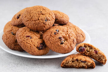 On a light background on a plate there are oatmeal cookies with dried cranberries.