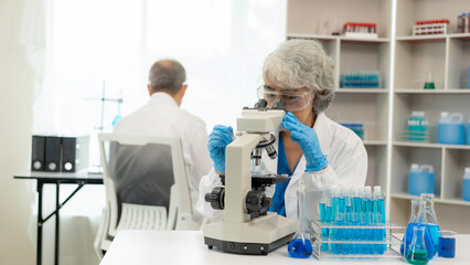 Fototapeta premium test tube microscope Two senior clinical workers, two men and women in the laboratory, two scientists doing research, young woman and her senior supervisor investigating with microscope and laptop.