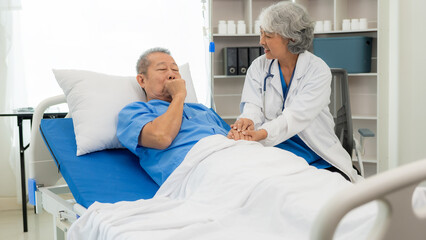 Senior Asian female nurse doctor visits a senior patient sitting on a patient's bed, explaining,...