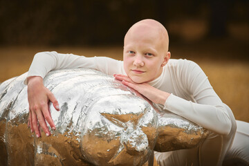 Portrait of young hairless girl with alopecia in white cloth hugging figure of tardigrade in autumn...