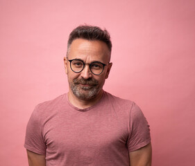 Portrait of mature 50s smiling caucasian man dressed in casual red t-shirt with glasses on calm attractive face isolated on pink studio background