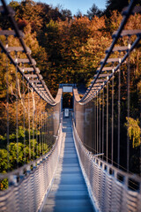 The warm, late-afternoon sun casts a golden glow over an empty suspension bridge, framed by the fiery colors of fall foliage, inviting a tranquil walk