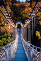 The warm, late-afternoon sun casts a golden glow over an empty suspension bridge, framed by the fiery colors of fall foliage, inviting a tranquil walk