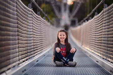 Seated in the heart of a suspension bridge, a joyful young girl laughs, her happiness amplified by...