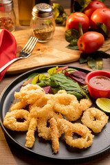 first plane Rings of squid with lemon on sause, on a wood background. Snack to beer or wine, Selective focus