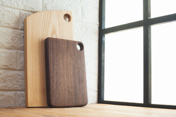 Wooden cutting boards leaning against the wall next to a window through which light enters.