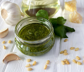 Sauce pesto in the glass jar and ingredients on the white wooden background. Close-up.