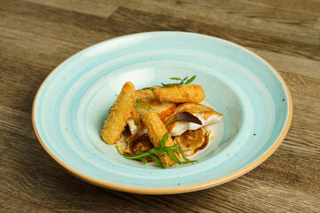Fried fish with baby corn in a plate on wooden table