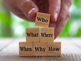 Hand stacking wooden blocks with text - How, Why, What, When, Where, Who. Fact finding concept