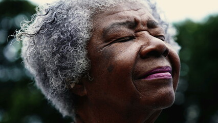 Grateful Senior African American woman closing eyes in Spiritual contemplation standing outside,...