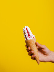 Strawberry ice cream cone in hand isolated on yellow background