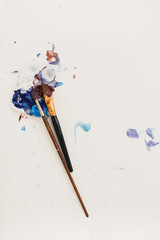 Paintbrushes with paint palette with splatters of paint colors smeared and isolated on a white background, creativity concept with copy space