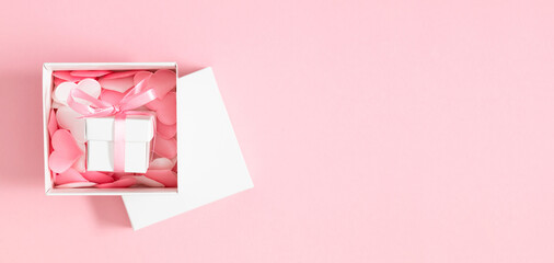 Pink background with pink and white hearts in an open gift box with a lid. Valentine's Day concept....