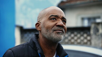 Pensive African American mature man in 50s observing urban surroundings while strolling in street,...