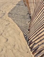 Crooked wooden beach fence with shadow pattern on beach sand