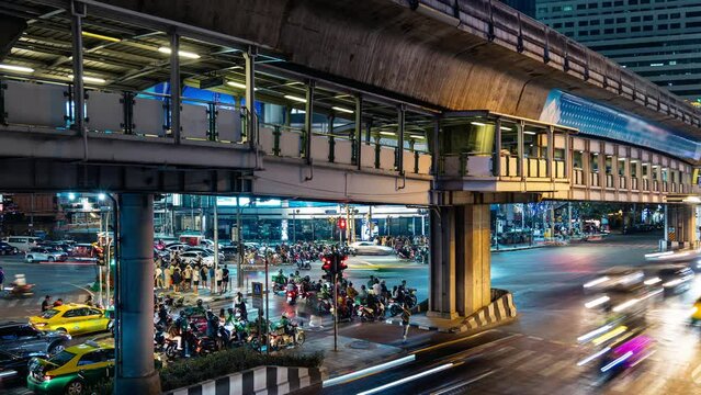 Vibrant nocturnal scene capturing the lively traffic and a moving train at an elevated station in Bangkok, showcasing urban transportation
