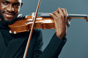 Elegant african american man playing violin in tuxedo on gray background for artistic music...