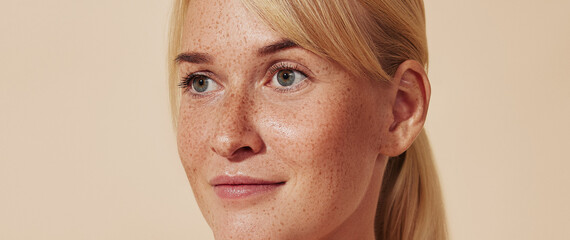 Cropped portrait of young blond woman with freckles. Female with smooth healthy skin against a...