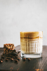 Dalgona coffee drink, cocktail with whipped instant coffee and milk in a glass on a wooden board with a healthy protein bar