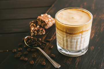 Dalgona coffee drink, cocktail with whipped instant coffee and milk in a glass on a wooden board with a healthy protein bar