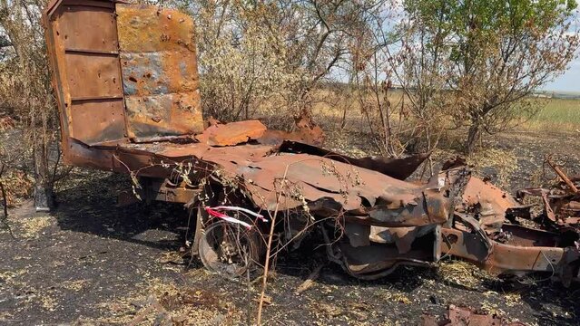 Truck burnt and rusted by fire against background of rusty parts from exploding ammunition, unsafe ammunition on field, charred by explosion. War in Ukraine