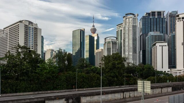 Urban landscape showcasing the diverse architecture of Kuala Lumpur's skyscrapers, interspersed with vibrant tropical foliage under a cloudy sky