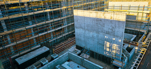 A construction site with scaffolding and a large concrete wall. Scene is one of progress and hard...