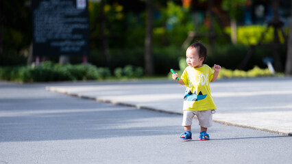 Portrait of a one-year-old Asian boy having fun walking among the playground. In the summer or spring, a child practices walking to develop and strengthen muscles.