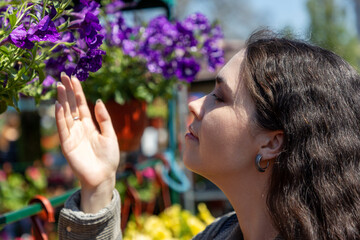 Close up of young Caucasian pretty woman smells fragrance of blooming flower in pots. Florist...
