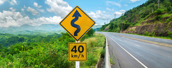 Warning traffic sign on metal pole winding road.