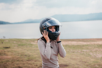 A female motorcyclist fastens her helmet against a serene lake backdrop