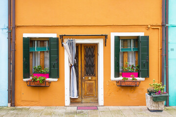 Murano and Burano island landscape. Venice region in Italy. Colorful various home facades. Orange paint house. Decorative flower plant pots and color paint window shutters. Italian architecture.	