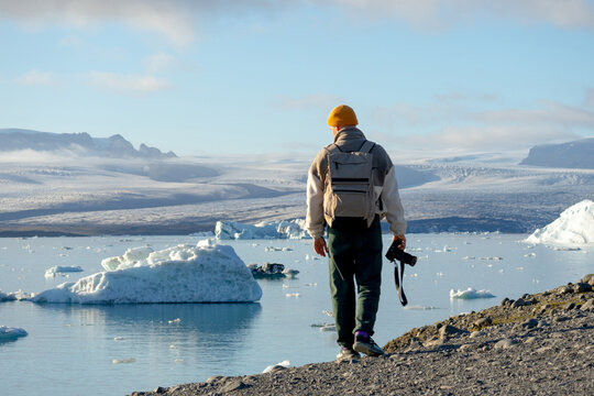 Young explorer with backpack,camera at glacier lagoon.Floating iceberg