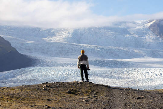 young man from behind holding camera in hands against huge glacier 